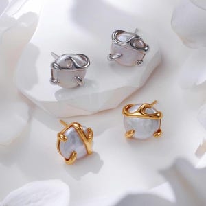 May include: Two pairs of pearl earrings with a unique, abstract design. One pair is silver and the other is gold.
