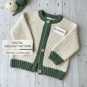 May include: Cream and green crochet cardigan with three buttons. The cardigan has a green trim around the collar, down the front, and on the cuffs and hem. The text "CROCHET" is on a tag attached to the cardigan. The text "DIGITAL CROCHET PATTERN INSTANT DOWNLOAD" is also visible.