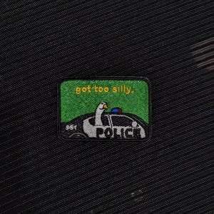 Può includere: Toppa ricamata con sfondo verde e la scritta "got too silly." La toppa presenta un'oca dei cartoni animati alla guida di un'auto della polizia. La parola "POLICE" è stampata sull'auto.