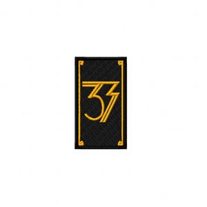 May include: A black rectangular patch with a gold-colored Art Deco design featuring the number "33". The patch has a gold border and is set against a white background.