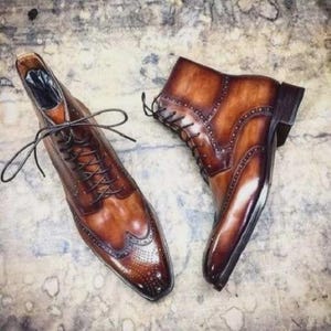 May include: A pair of brown leather dress boots with intricate detailing. The boots feature a classic lace-up design, brogue accents, and a polished finish. The footwear is designed for formal occasions.