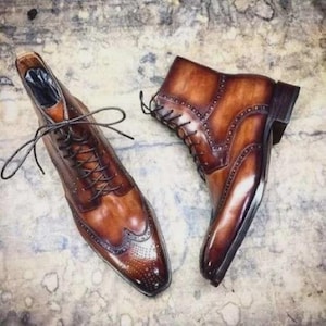 May include: A pair of brown leather dress boots with intricate detailing. The boots feature a classic lace-up design, brogue accents, and a polished finish. The footwear is designed for formal occasions.