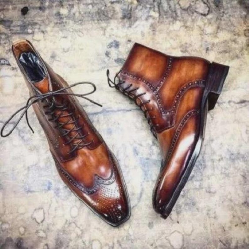May include: A pair of brown leather dress boots with intricate detailing. The boots feature a classic lace-up design, brogue accents, and a polished finish. The footwear is designed for formal occasions.