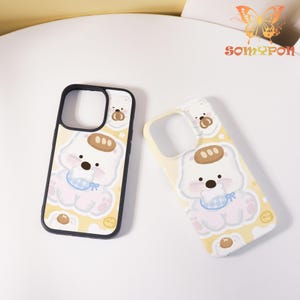 May include: Two phone cases with a cute cartoon bear design. The cases are yellow with a black border and feature a white bear with a blue bib. The bear has a brown bread-like shape on its head and is surrounded by stars and small circles.