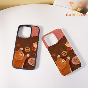 May include: Two phone cases with a brown design featuring a cartoon cat, coffee cup, and pastries. The cases have a black border and a pink scalloped top. The brand name "SOMYPON" is visible in the upper right corner.