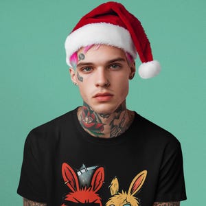 May include: A person wearing a black t-shirt with a cartoon rabbit graphic and a Santa hat. The graphic features two rabbits, one red and one yellow, with a Christmas theme. The background is a solid teal color.