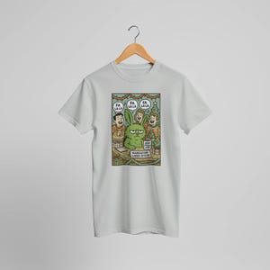 May include: White t-shirt featuring a cartoon illustration of a grumpy green bunny wearing a name tag that says "Mandatory Cheer Officer." The bunny is surrounded by people singing "Fa La La La."