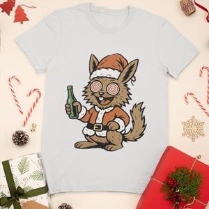 May include: A light gray t-shirt featuring a cartoon rabbit dressed as Santa Claus, holding a green bottle. The rabbit has spiral eyes and is wearing a Santa hat and suit. The words "Merry Christmas" are at the bottom.