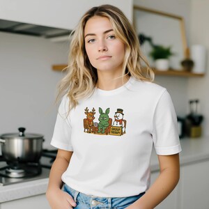 May include: White t-shirt featuring a cartoon illustration of a reindeer, a green rabbit, and a snowman in a group therapy session. The text "GROUP THERAPY" is on a sign in front of them.