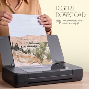 May include: A landscape art print featuring a desert scene with tan mountains and green foliage is held above a black printer. The print is labeled "DIGITAL DOWNLOAD" with instructions to download, print, frame, and enjoy.