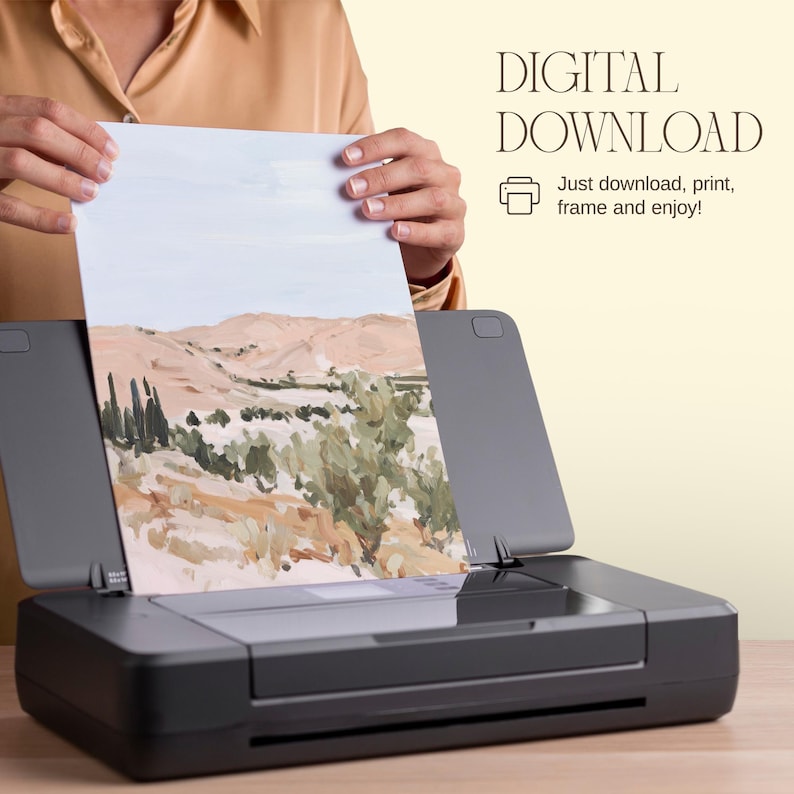 May include: A landscape art print featuring a desert scene with tan mountains and green foliage is held above a black printer. The print is labeled "DIGITAL DOWNLOAD" with instructions to download, print, frame, and enjoy.