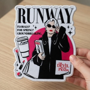 May include: A white and black patch with the word "RUNWAY" at the top. The patch features a woman in sunglasses, a coffee cup, a book, and the text "THE DEVIL WEARS PRADA". The background is pink.