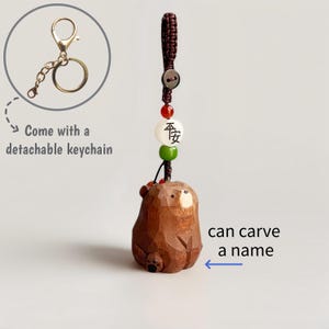 May include: A brown wooden bear keychain with a detachable gold-colored keychain. The bear has a carved design and is attached to a cord with beads. The text "can carve a name" is visible.