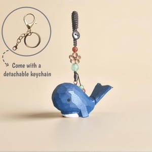 Peut inclure: Un porte-clés en forme de baleine en bois bleu avec un porte-clés détachable de couleur or. La baleine a un ventre blanc et une queue bleu foncé. Le porte-clés est orné de perles et d'un charm en forme de fleur.