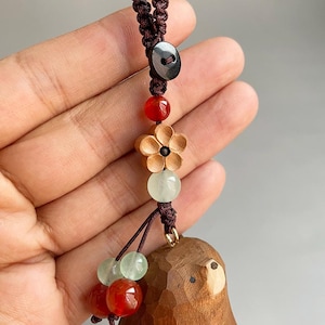 May include: A wooden bear pendant with a brown cord, adorned with red, green, and wooden beads. The pendant features a carved bear design and a small black button. The cord is knotted and appears to be made of a dark brown material.