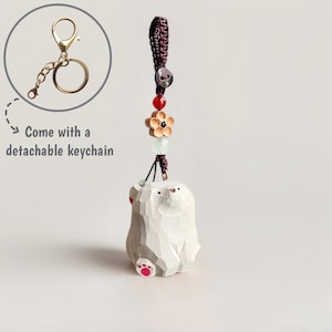 May include: A carved wooden bear keychain with a detachable gold-colored keychain. The bear is white with red accents on its paws and ears. The keychain has a decorative cord with beads and a flower charm. The text "Come with a detachable keychain" is also present.