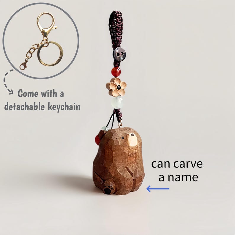 May include: A brown, carved wooden bear keychain with a detachable gold-colored keychain. The bear has a detailed, textured surface and is adorned with decorative beads and a flower. Text on the image says "can carve a name".