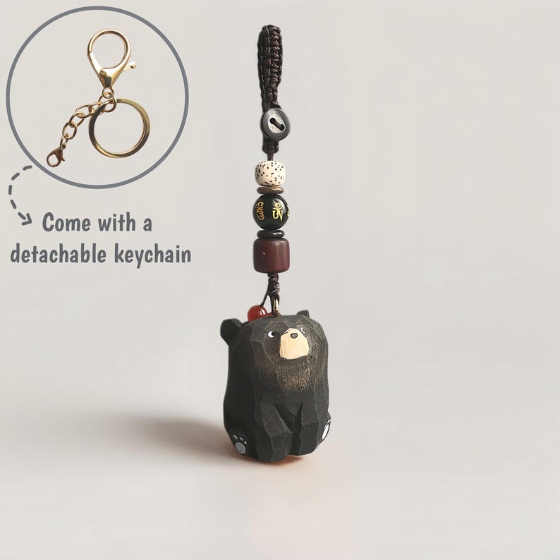 May include: A black wooden bear keychain with a detachable gold-colored keychain. The bear is carved with a sitting pose and has a light brown face. The keychain includes decorative beads and a braided cord.