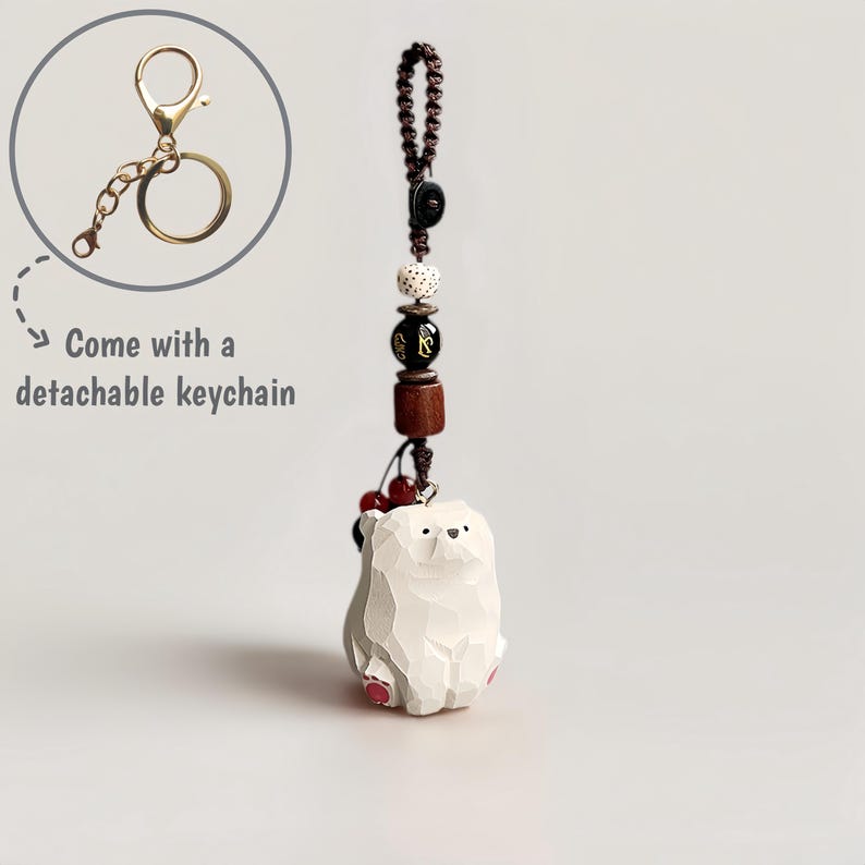 May include: A white bear keychain with a detachable gold-colored keychain. The bear has a carved appearance with pink accents on its feet. The keychain includes a beaded strand with wooden and decorative beads. The text "Come with a detachable keychain" is also visible.