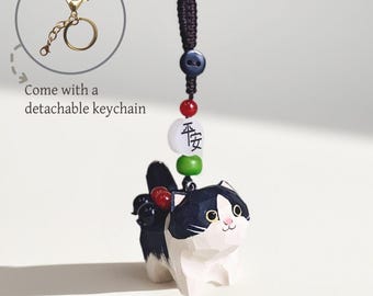 May include: A wooden cat figurine with black and white markings, a beaded charm, and a detachable gold-coloured keychain. The cat has a smiling expression and is adorned with red and green beads. The charm has Chinese characters.