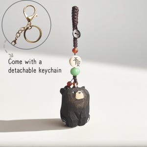 Peut inclure: Un porte-clés ours en bois noir avec un porte-clés détachable de couleur or. L'ours a un visage de couleur claire et est attaché à un cordon avec des perles. Le texte "Come with a detachable keychain" est dans l'image.
