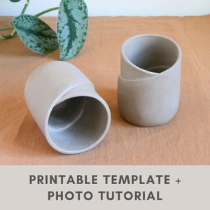 May include: Two beige ceramic planters with a distinctive curved design. One planter is on its side, the other upright. The planters are on a light brown surface, with green and silver leaves in the background. The text "PRINTABLE TEMPLATE + PHOTO TUTORIAL" is at the bottom.