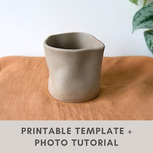 May include: A handmade, light beige ceramic cup with an organic, asymmetrical shape. The cup has a smooth, unglazed finish and a slightly irregular rim. The text "PRINTABLE TEMPLATE + PHOTO TUTORIAL" is at the bottom of the image.