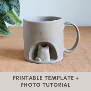 May include: A beige ceramic mug with a cat design. The mug has a cat figure inside a cutout. The handle is a curved loop. The text "PRINTABLE TEMPLATE + PHOTO TUTORIAL" is at the bottom.