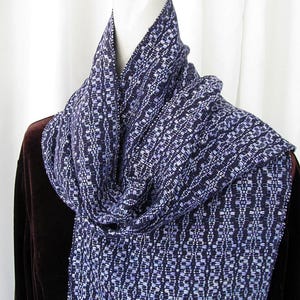 May include: A blue and white woven scarf with a geometric pattern. The scarf is draped around a white mannequin's neck.