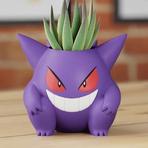 Puede incluir: Maceta de Pokémon fantasma púrpura con una planta suculenta verde en su interior.