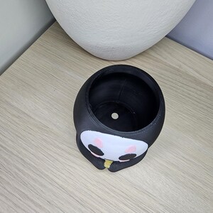 May include: Black and white planter shaped like a cartoon character with a round head and a small mouth. The planter has a small hole in the bottom for drainage.