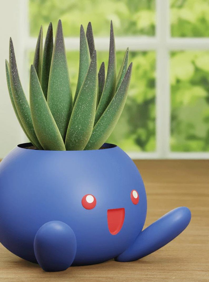 May include: A blue and red cartoon planter shaped like a Pokemon character with a green succulent plant inside.