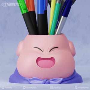 Puede incluir: Un organizador de escritorio rosa y morado con forma de personaje de dibujos animados con una cara sonriente. El organizador tiene una boca ancha y contiene una variedad de bolígrafos y lápices.