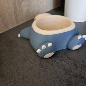 May include: A blue and white ceramic planter shaped like a cartoon character. The planter has a round opening at the top for planting.