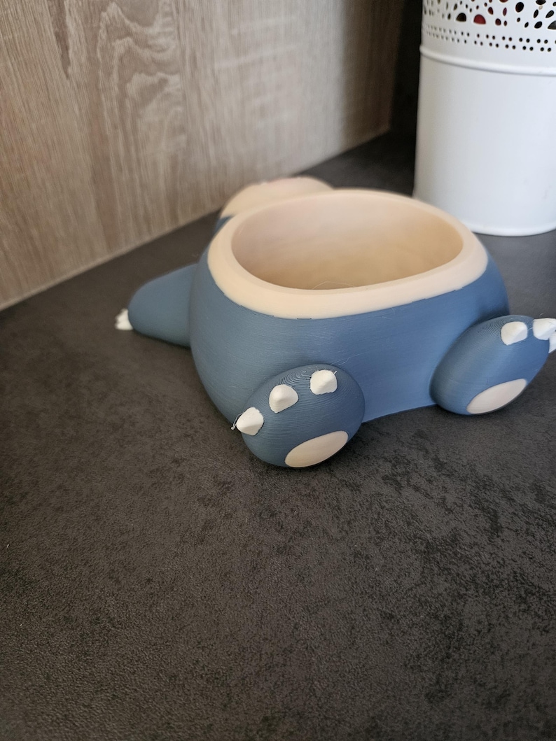 May include: A blue and white ceramic planter shaped like a cartoon character. The planter has a round opening at the top for planting.