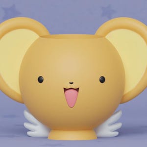 May include: A yellow ceramic planter shaped like a cartoon character with large ears, a smiling face, and a pink tongue sticking out. The planter has white wings on each side.