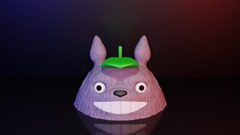 Może przedstawiać: Rendowana w 3D figurka przypominająca Totoro. Figurka jest gł&oacute;wnie lawendowa z teksturowaną powierzchnią, dużymi białymi zębami i zielonym liściem na głowie. Oczy są czarno-białe, na ciemnym tle.