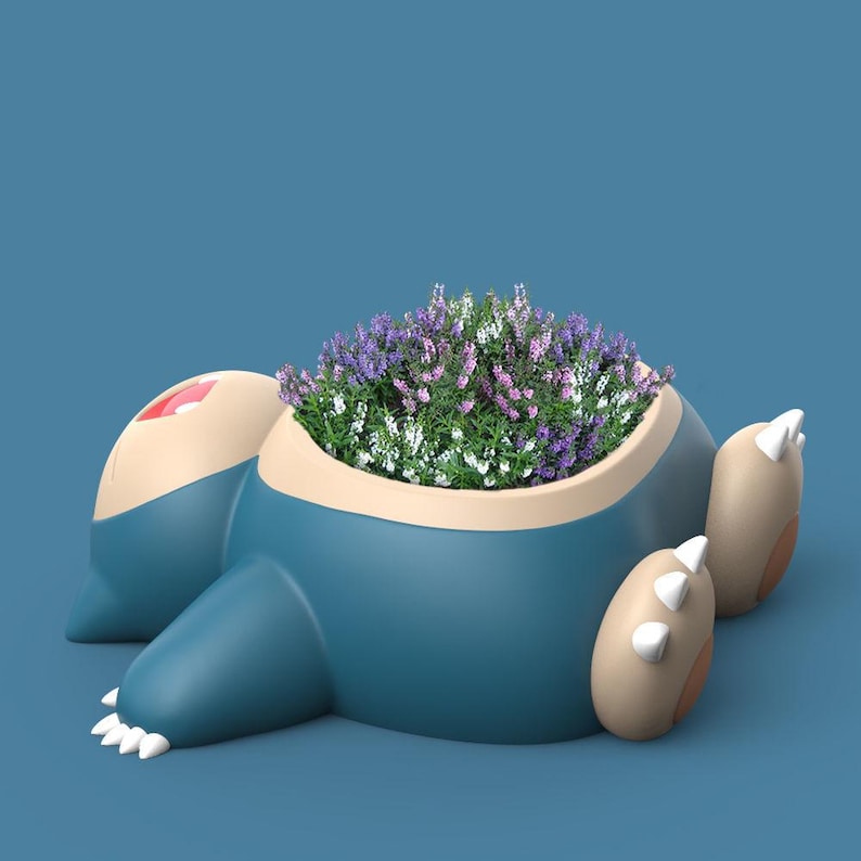 May include: A blue and brown ceramic planter shaped like a cartoon character with purple and white flowers growing inside.
