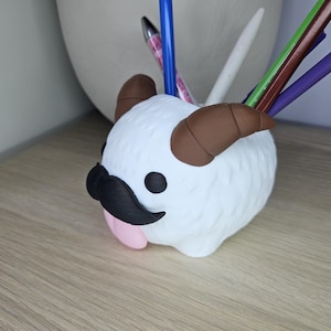 May include: White fuzzy pen holder shaped like a cartoon character with brown horns, a black mustache, and a pink tongue sticking out.