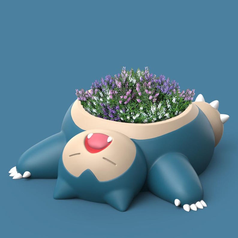 May include: A blue and brown ceramic planter shaped like a cartoon character with a smiling face. The planter is filled with purple and white flowers.
