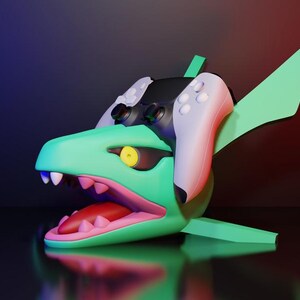 May include: A stylized, 3D-rendered sculpture of a shark-like creature with a gaming controller integrated into its design. The sculpture is primarily green with white teeth, a pink mouth, and a yellow eye. The controller is black and white. The background is a gradient of blue and red.