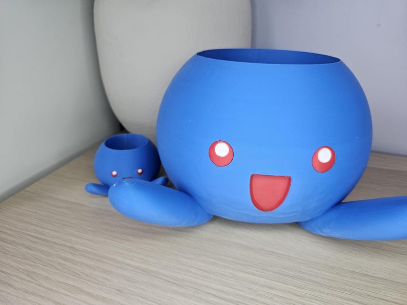 May include: Two blue ceramic octopus planters with red smiling faces. The larger planter has a wider opening and the smaller planter has a narrower opening.