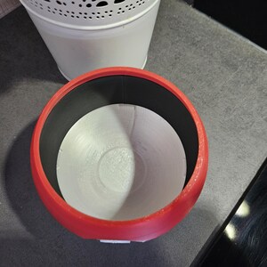 May include: A red ceramic planter with a white interior and a black rim. The planter is empty and ready for a plant.