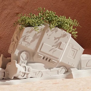 Può includere: Un vaso da fiori in ceramica bianca a forma di AT-ST Walker di Star Wars con piante verdi che crescono dalla cima.