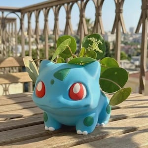 May include: A light blue creature-shaped planter with large red eyes, dark green spots, and white claws. The planter features a hollow opening on its back containing a green Pilea peperomioides plant with round leaves and small white flowers.