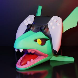 Könnte beinhalten: Ein grüner und weißer Gaming-Controller-Ständer in Form eines Dinosaurierkopfes mit offenem Maul. Der Ständer hält einen schwarz-weißen Controller. Der Dinosaurier hat ein gelbes Auge und weiße Zähne. Der Ständer steht auf einer reflektierenden Oberfläche.