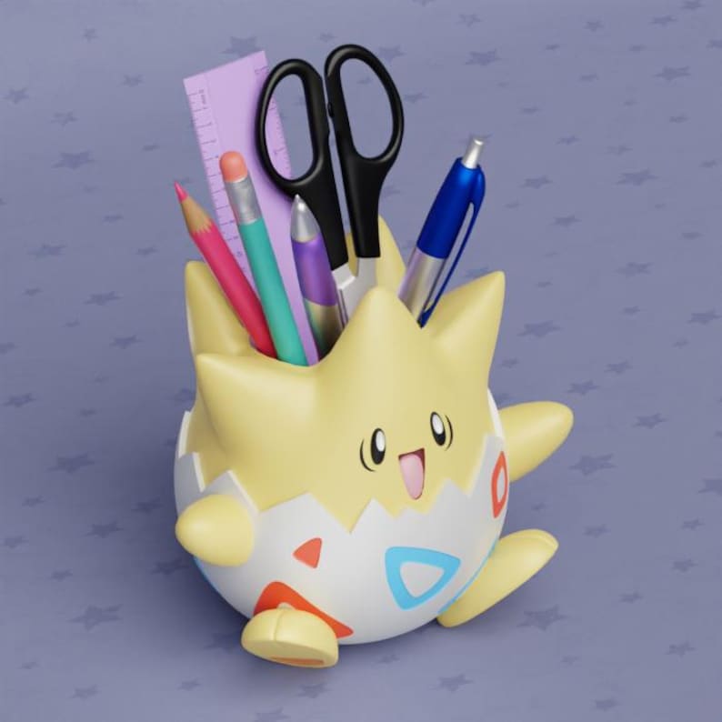 May include: A yellow and white character-shaped desk organizer holding school supplies. The organizer has a smiling face and holds a pink pencil, a teal pencil, a purple pen, black scissors, a blue pen, and a purple ruler.