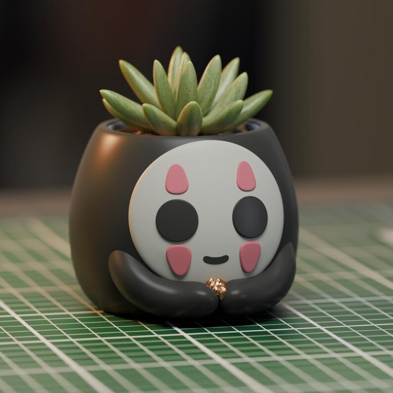 May include: A black and white ceramic planter shaped like a character from the movie Spirited Away. The planter has a green succulent plant growing inside.