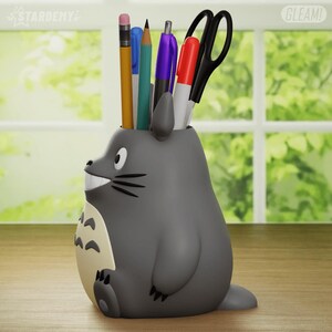 May include: Gray Totoro-shaped desk organizer with a smiling face and a white belly. The organizer is filled with pencils, pens, and a pair of scissors.