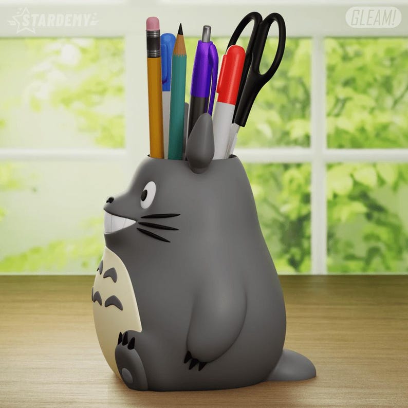 May include: Gray Totoro-shaped desk organizer with a smiling face and a white belly. The organizer is filled with pencils, pens, and a pair of scissors.